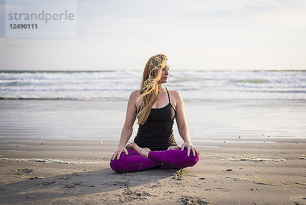 Frau sitzt am Strand und macht Yoga in Rhode Island an einem windigen Tag