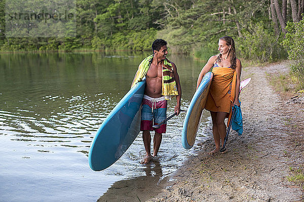 Junges Paar trägt ihr Paddleboard in der Nähe von Teich