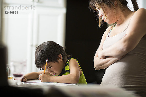 Ein japanischer Junge lernt in einer Küche japanische Hausaufgaben  während seine Mutter zusieht.