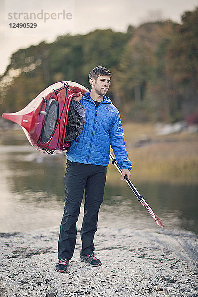 Ein junger Mann trägt sein Kajak entlang der felsigen Küste von Maine