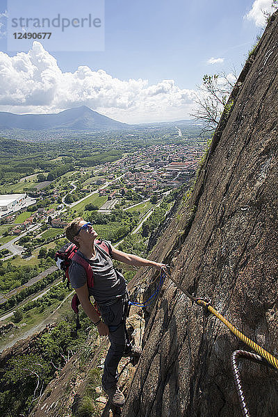Junger Mann steigt über einen Klettersteig auf  unten im Tal