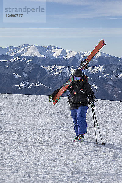 Skifahrer  der auf den Gipfel des Berges zugeht und seine Skier auf der Schulter trägt