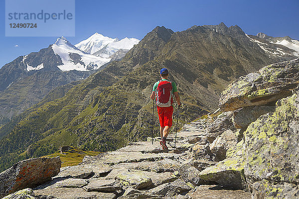 Ein Wanderer auf einem felsigen historischen Handelsweg mit dem Weisshorn über dem Matterhorntal