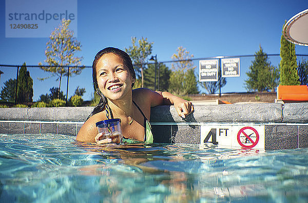 Lächelnde asiatische Frau mit ihrem Getränk im Pool