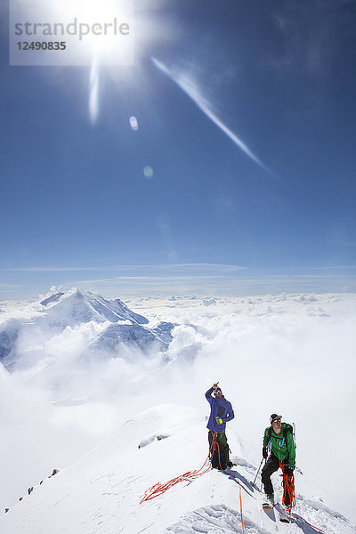 Die Bergsteiger und Ranger Dave Weber und Tom Ditolla befinden sich auf einem Schneegrat der Westrippe hoch auf dem Mount McKinley. Dave zeigt auf den Gipfel des McKinley  Mount Hunter ist im Hintergrund zu sehen. Der Mount McKinley oder Denali ist der höchste Berg Nordamerikas mit einer Gipfelhöhe von 6.168 m (20.237 Fuß) über dem Meeresspiegel. Mit einer Höhe von rund 5.500 m (18.000 Fuß) ist er der höchste Berg  der vollständig über dem Meeresspiegel liegt. Gemessen an der topografischen Ausdehnung ist er nach dem Mount Everest und dem Aconcagua der drittgrößte Berg. Der McKinley befindet sich in der Alaska Range im Inneren des US-Bundesstaates Alaska und ist das Herzstück des Denali National Park and Preserve.