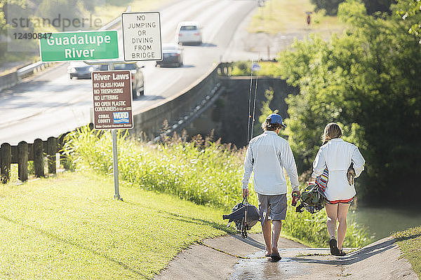 Ein Mann und eine Frau mit ihrem Hund gehen in Richtung des Guadalupe River zum Fliegenfischen