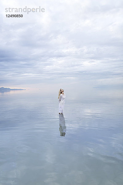 Eine junge Frau steht in einem See mit einem weiten Himmel.