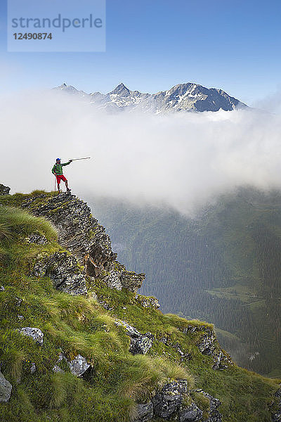 Wanderung auf steilem Grat  mit Wanderstock auf Bergkette im Hintergrund zeigend