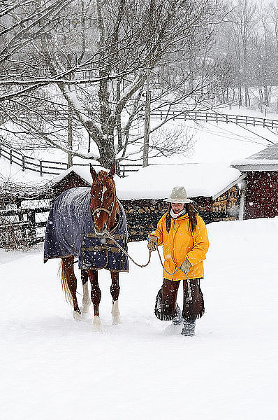 Frau steht mit ihrem Pferd in verschneiter Landschaft