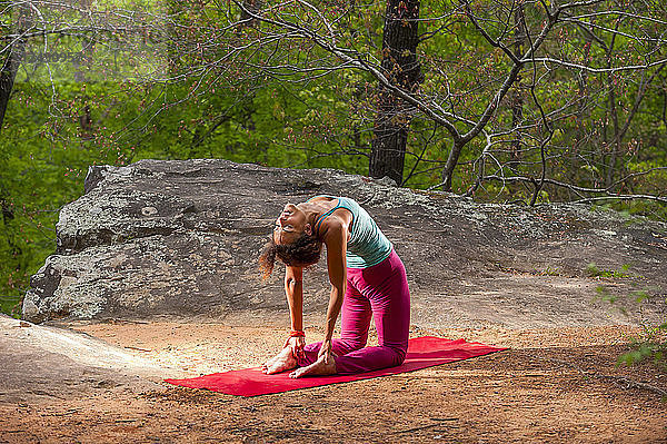 Frau macht Stretching auf Yoga-Matte im Wald