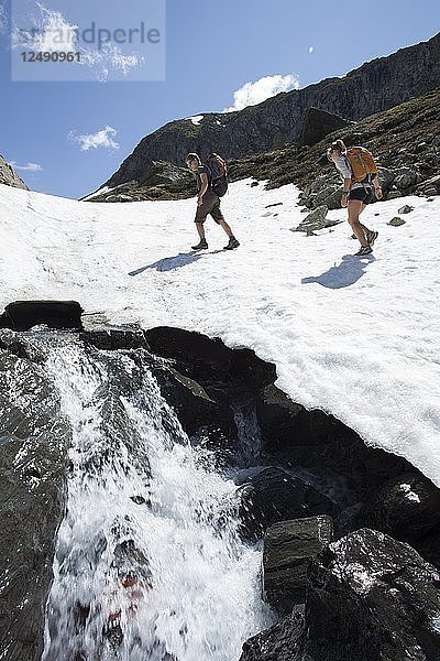 Junges Wandererpaar steigt einen Schneehang oberhalb eines Baches hinauf