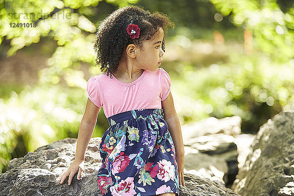 Ein kleines Mädchen sitzt auf den Felsen entlang eines Baches.
