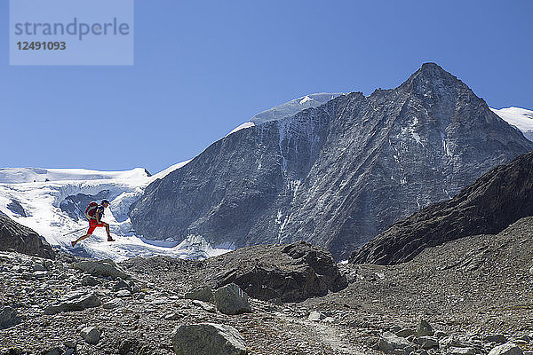 Ein männlicher Wanderer springt vor dem Mont Blanc de Cheilon  einem Berg am Ende des Val d'H?©r?©mence in der Schweizer Region Wallis  fröhlich in die Luft. Dieser liegt auf halbem Weg der Haute Route  einer beliebten alpinen Wanderung durch Frankreich und die Schweiz.