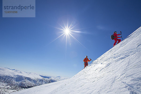 Zwei Skifahrer stehen auf einem verschneiten Berg in der Nähe des Skigebiets von Myrkdalen in Fjord  Norwegen. Die Sonne scheint hell am blauen Himmel. Mit 5 Metern jährlichem Schneefall  allen Arten von Gelände und effizienten Skiliften sind Sie bestens gerüstet für einen herrlichen Skiurlaub in Myrkdalen. Das familienfreundliche Myrkdalen liegt in Voss 'Äì nur zwei Stunden vom internationalen Flughafen Bergen mit Direktflügen von Kopenhagen  Amsterdam und London entfernt. Myrkdalen ist das größte Skigebiet in Westnorwegen - mit familienfreundlichen Skigebieten  Pisten aller Schwierigkeitsgrade  Terrainparks  Skicross-Pisten und großartigem Gelände abseits der Pisten. In der Nähe des Skigebiets gibt es präparierte Langlaufloipen und großartiges Terrain für Backcountry-Skiing. '