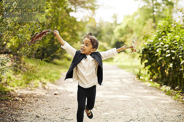 Ein kleines Mädchen  das mit zwei großen Blättern auf einer Schotterpiste läuft
