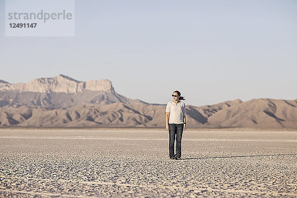 Eine junge Frau  die auf einer Salzebene in Texas mit Guadalupe Peak im Hintergrund steht