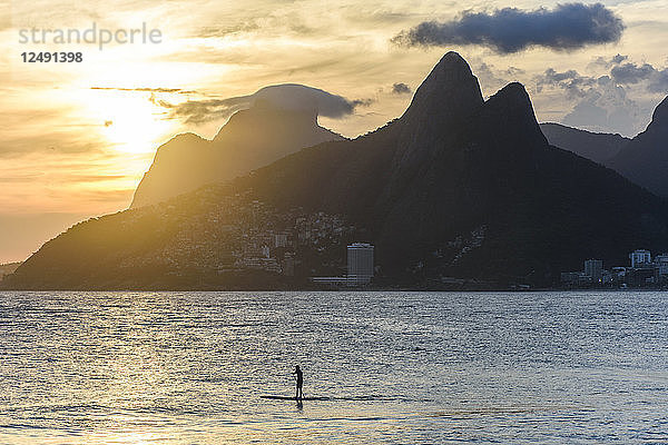 Einheimischer auf einem Stand Up Paddle Board bei Sonnenuntergang am Strand von Ipanema  Morro Dois Irmaos im Hintergrund  Rio de Janeiro  Brasilien