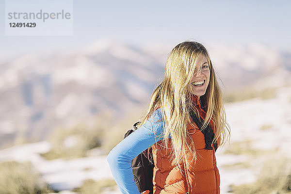 Eine junge Frau mit blondem Haar lächelt bei einer Winterwanderung.