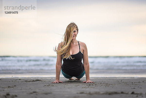 Eine Frau macht Yoga am Strand in Rhode Island an einem windigen und bewölkten Tag