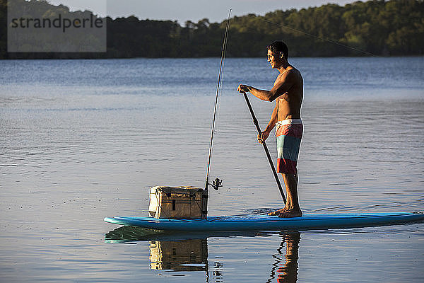 Junger Mann mit seiner Angelausrüstung auf einem Stand Up Paddle Board