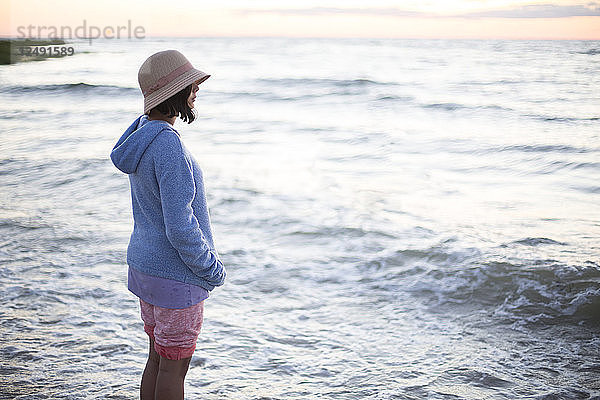 Frau mit Sommerhut am Strand stehend