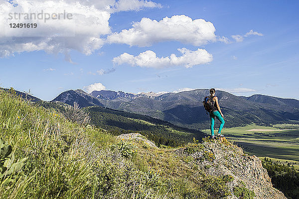 Eine Frau macht eine Wanderpause und stellt sich auf einen Felsvorsprung  um den Blick auf die gewaltige Berglandschaft Montanas zu richten.