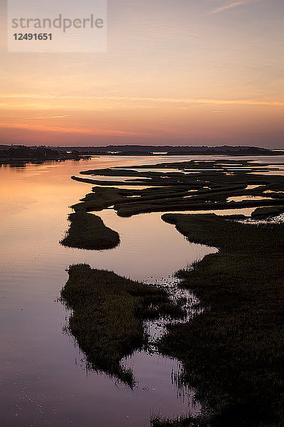 Frühlingssonnenaufgang über dem ICW und dem Sund zwischen dem Festland und den NC Barrier Islands. Schilf unterbricht den Vordergrund  während sich der frühe Morgenhimmel über dem Wasser spiegelt.