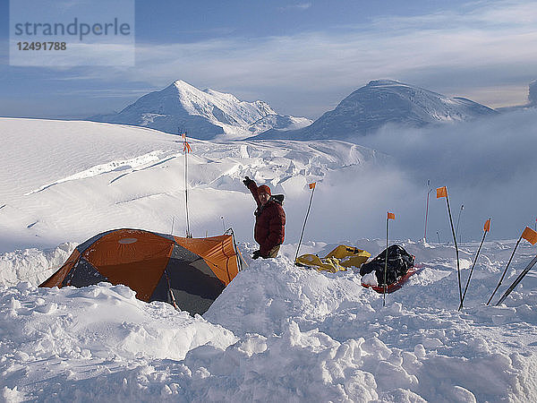 Der Bergsteiger und Ranger Brian Scheele steht neben seinem Zelt und zeigt vom 12.000 Fuß hohen Camp auf dem Mount McKinley auf den Mount Foraker. Der Mount McKinley oder Denali ist der höchste Berg Nordamerikas mit einer Gipfelhöhe von 6.168 m (20.237 Fuß) über dem Meeresspiegel. Mit einer Höhe von rund 5.500 m (18.000 Fuß) ist er der höchste Berg  der vollständig über dem Meeresspiegel liegt. Gemessen an der topografischen Ausdehnung ist er nach dem Mount Everest und dem Aconcagua der drittgrößte Berg. Der McKinley befindet sich in der Alaska Range im Inneren des US-Bundesstaates Alaska und ist das Herzstück des Denali National Park and Preserve.