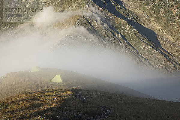 Zelte in alpiner Umgebung bei Sonnenaufgang in Nebel gehüllt