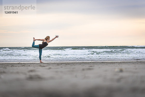 Eine Frau  die Yoga an einem bewölkten Tag am Strand von Rhode Island macht