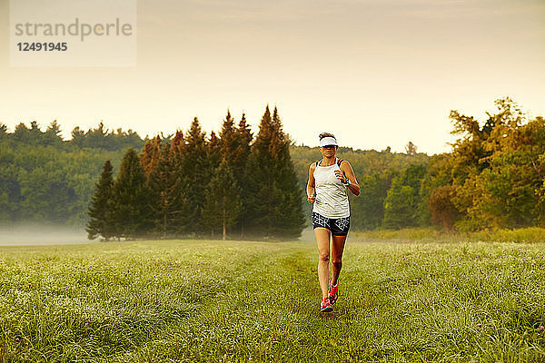 Weibliche Läuferin läuft auf grasbewachsenen Landschaft während einer nebligen Morgen