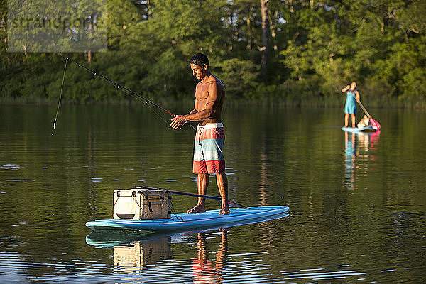 Junger glücklicher Mann beim Fliegenfischen auf einem Paddleboard