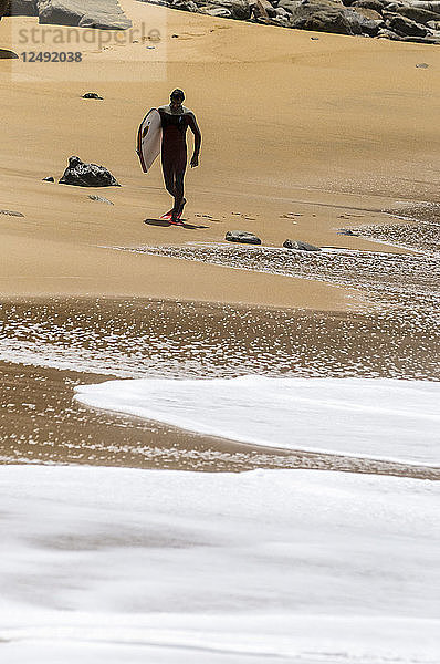 Bodyboarder  der nach einer Surfsession am Strand spazieren geht.