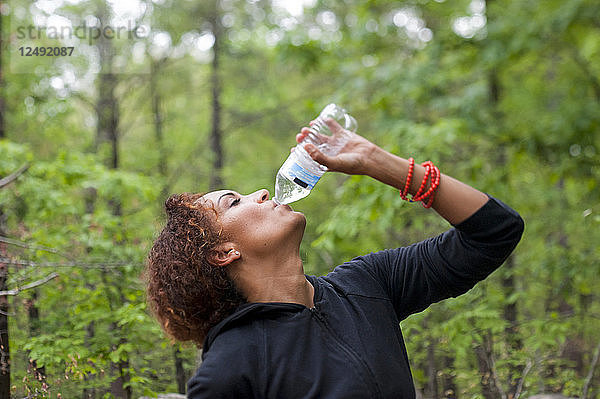 Nahaufnahme einer Frau  die Wasser aus einer Flasche im Wald trinkt