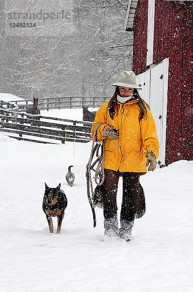 Frau geht mit ihrem Hund in verschneiter Landschaft spazieren