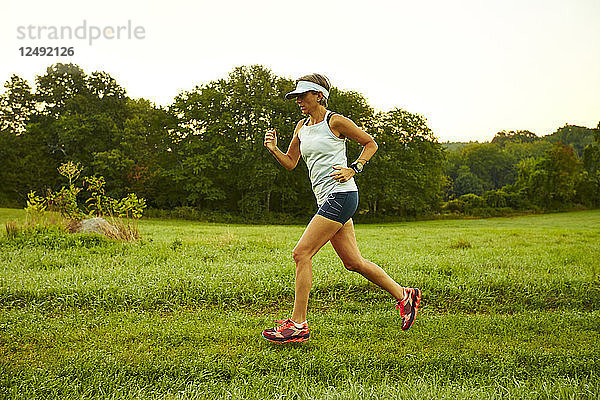 Weibliche Läuferin läuft durch ein Feld an einem nebligen Morgen