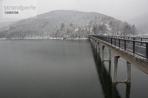 Einspurige Brücke über Bergsee  ferne Hügel und Sturm