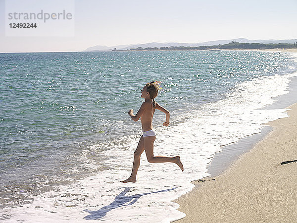 Junges Mädchen rennt ins Meer mit der Küstenlinie im Rücken