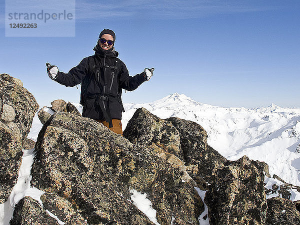 Lächelnder junger Mann  der auf dem Gipfel des Cerro Catedral einen doppelten Daumen nach oben streckt