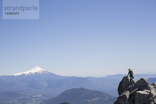 Wanderer klettert auf Felsbrocken mit schneebedecktem Vulkan im Hintergrund