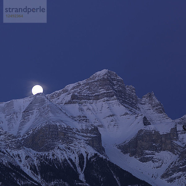 Der Vollmond steht über dem schneebedeckten Gipfel