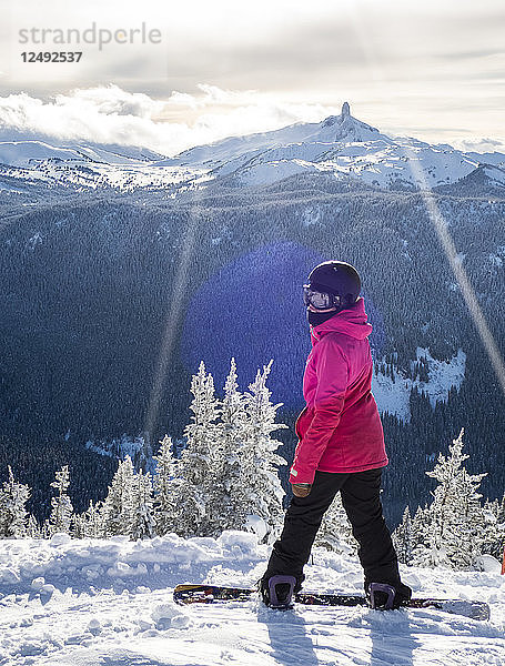 Eine Snowboarderin macht eine Pause und blickt auf die Aussicht auf Black Tusk vom Whistler Blackcomb Ski Resort hinaus