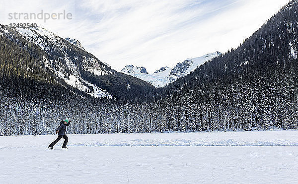 Ein Mädchen läuft an einem kalten Wintertag auf dem Joffre Lake in British Columbia Schlittschuh