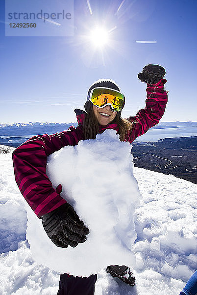 Männlicher Skifahrer  der mit einem Arm einen Schneeblock hält und sich mit dem anderen beugt  in Argentinien