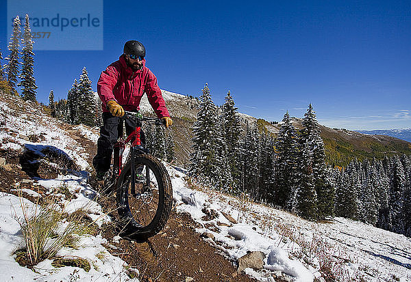 Ein rot gekleideter Mann fährt im Herbst auf einem verschneiten Weg in Utah mit einem Fahrrad mit großen Reifen.