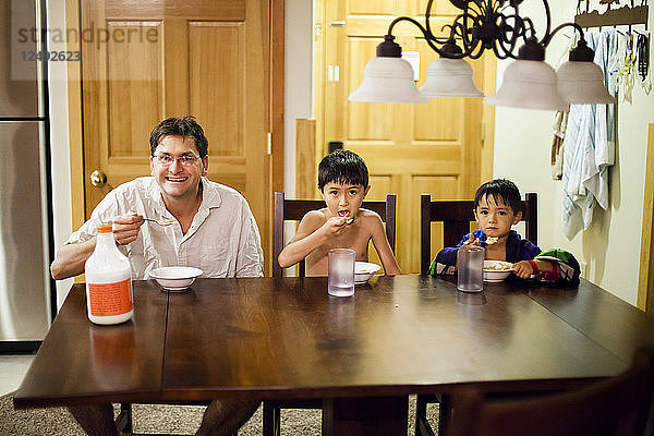 Ein Vater und seine sieben und vier Jahre alten Söhne essen im Urlaub am Tisch Müsli.