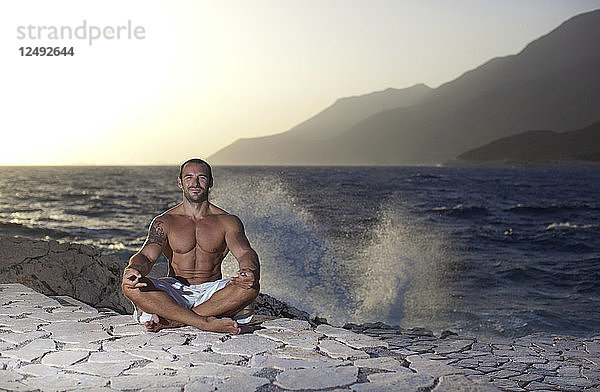 Muskulöser Mann meditiert in einer Yoga-Pose  in der Nähe des Meeres. Ka?ü Antalya Türkei