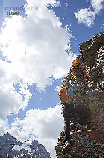 Bergführer hilft einer Bergsteigerin beim Aufstieg über die Felswand