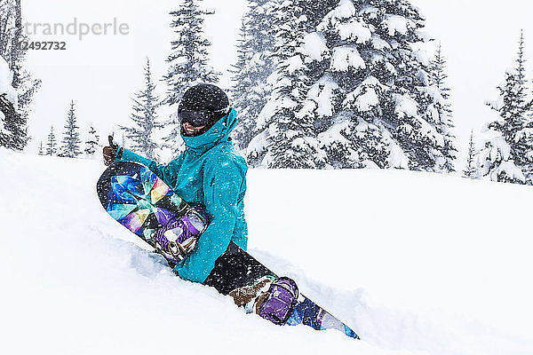 Ein weiblicher Snowboarder wandert durch hüfttiefen Schnee und gibt einen Daumen hoch im Whistler Blackcomb Ski Resort