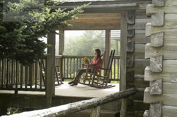 Eine Frau in einem Schaukelstuhl liest auf der Veranda einer Hütte der Leconte Lodge  Mount Leconte  Great Smoky Mountain National Park  Gatlinburg  Tennessee.
